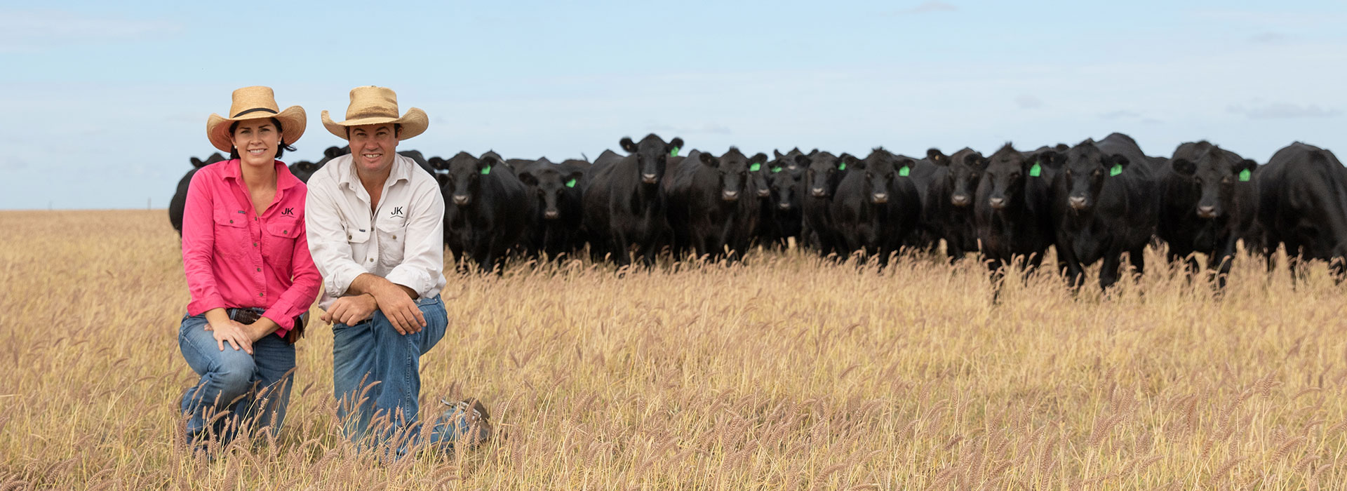 Justin and Kate Boshammer kneeling in front of Angus cattle